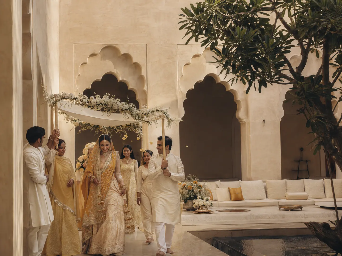 A bride arriving beneath a floral canopy in a quiet Udaipur courtyard